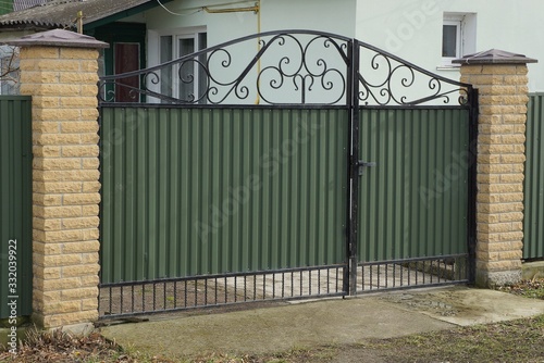 Fototapeta Naklejka Na Ścianę i Meble -  one large green metal gate and part of a brown brick fence in the street