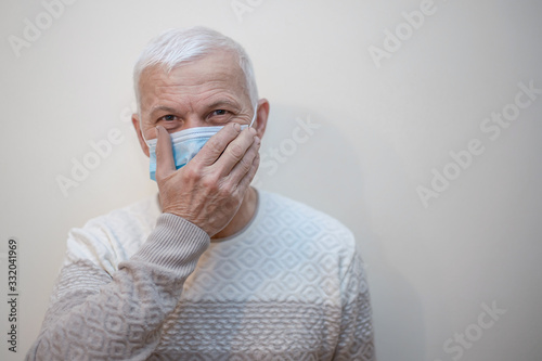 Elderly man in protective medical mask isolate in white. Coronavirus elderly advice. Safety old men. Copy space. man touches face with hand. Mistakes in wearing protective masks