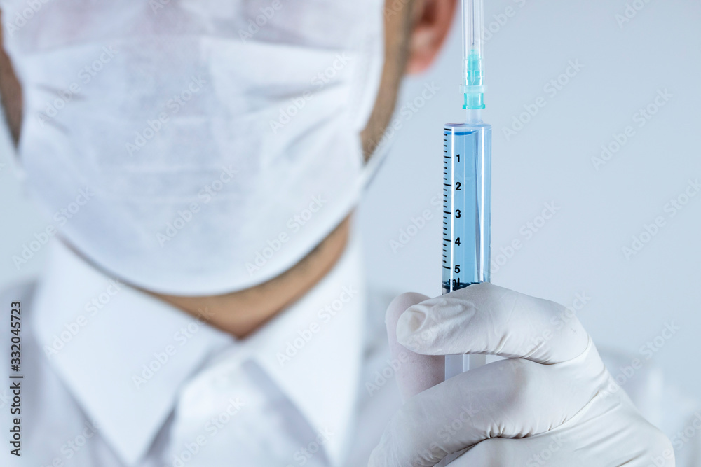 The doctor is holding the syringe with blue liquid in the glove. Close-up. Syringe focused. The doctor is holding the syringe with blue liquid in the glove. Close-up. Syringe focused.