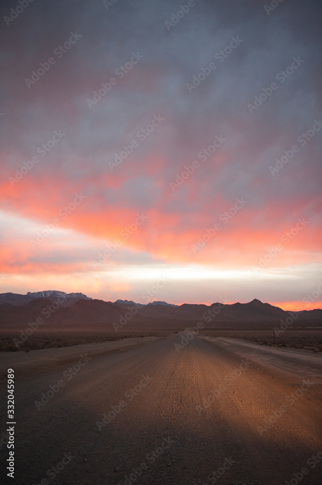Headlights shining on a desert road under a sunset lit cloudy sky