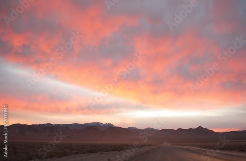Headlights shining on a desert road under a sunset lit cloudy sky