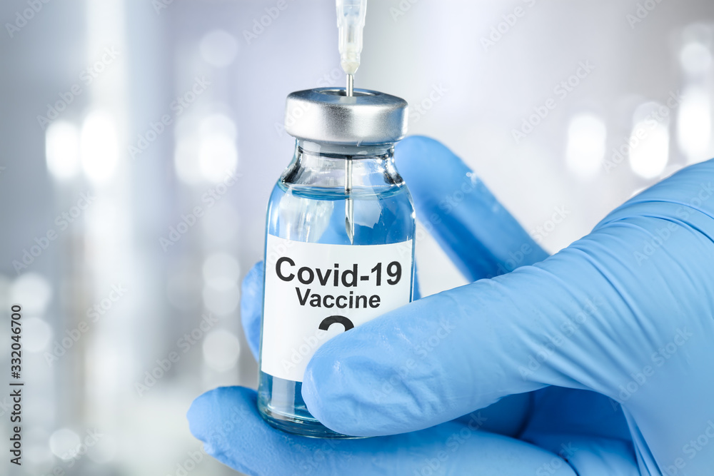Possible cure concept with a hand in blue medical gloves holding Coronavirus, Covid 19 virus, vaccine vial