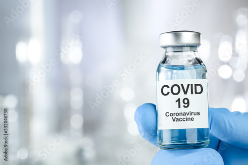 Healthcare cure concept with a hand in blue medical gloves holding Coronavirus, Covid 19 virus, vaccine vial