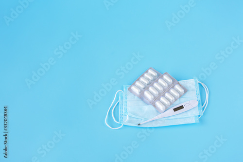  Face mask, thermometer, pills on a blue background. Medicine supplies for home coronavirus COVID-19 quarantine. Copy Space