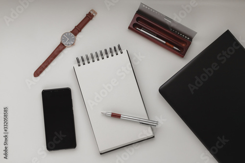 Minimalist workspace background with laptop, pen, pen case, wrist watch and open notebook. White office desk frame