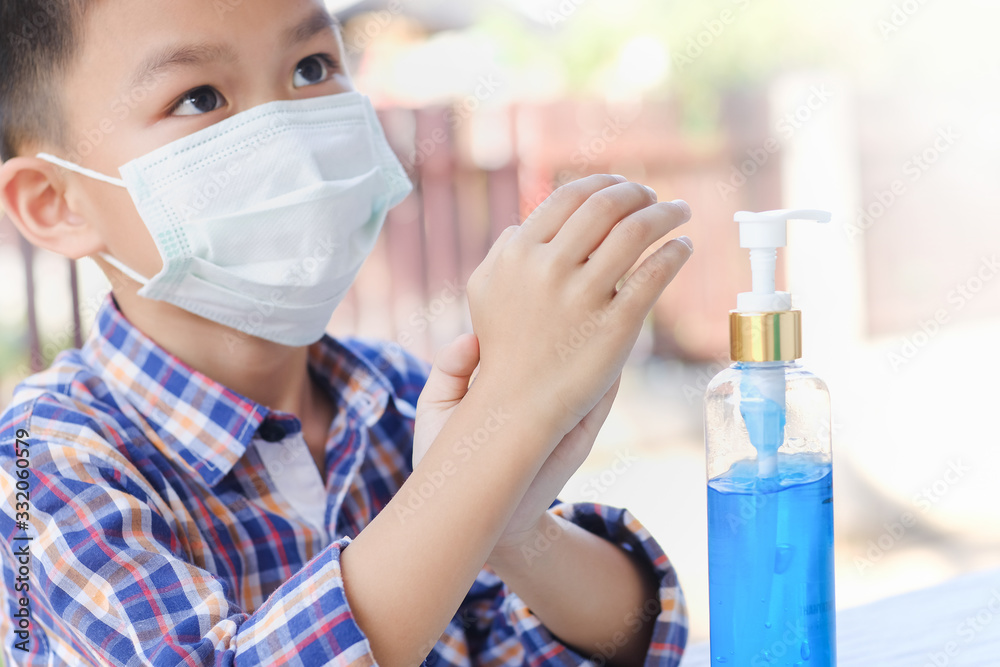 Asian boy wearing medical mask using hand sanitizer.