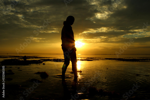 Fotografie Person walking on the beach at sunrise.