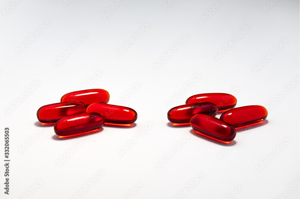 Two small piles of red capsule tablet pills medication on plain white background. Cure and treatment concept. Two small piles of red capsule tablet pills medication on plain white background. Cure and treatment concept.