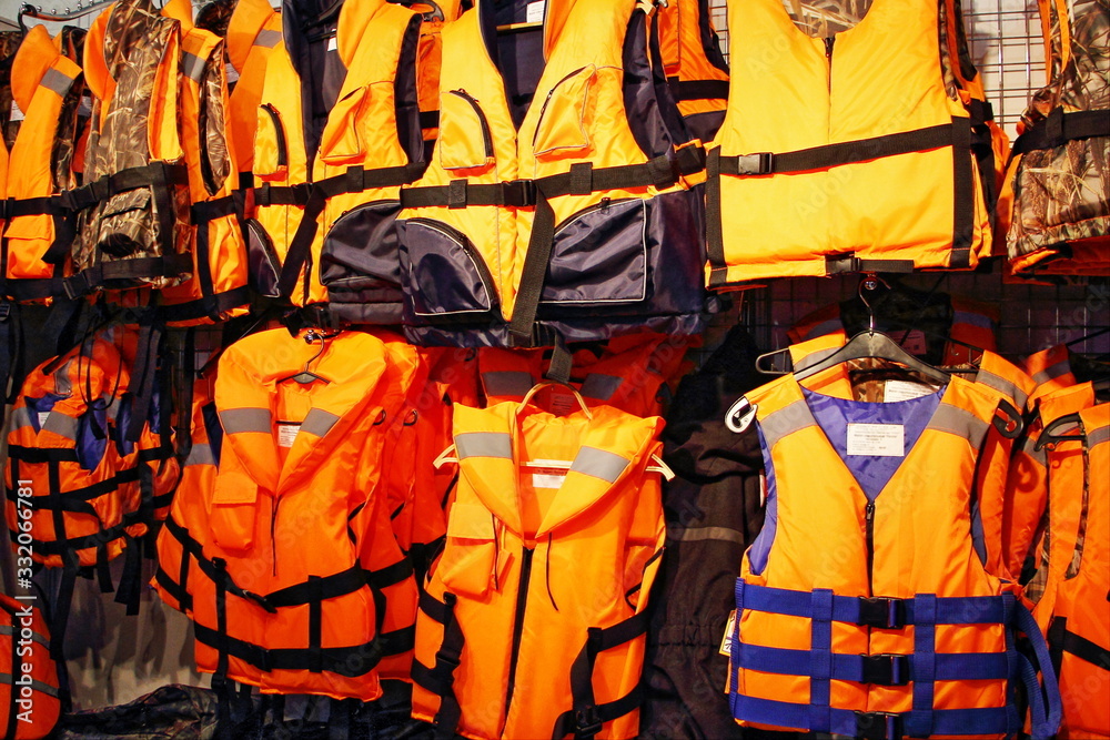 A many bright orange marine life vest jackets on rack in shop, safety on water tourism activity and watersports