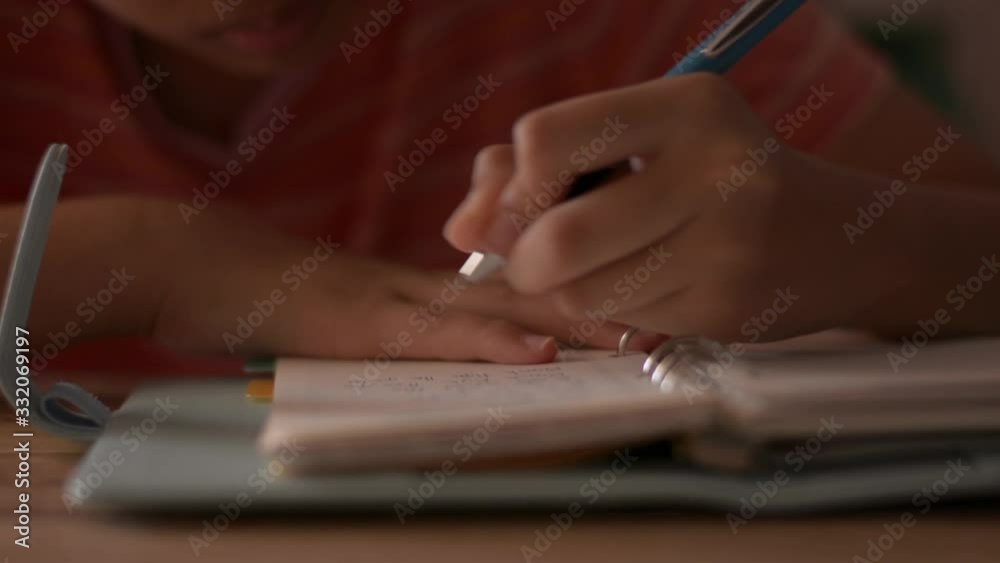 Close up hand of a little girl writing on notebook. Female schoolchild making notes on a diary. Doing homework with writing material. Education concept.