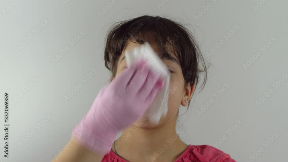 A teenage girl stands on a light background. A female hand in a glove wipes a girl's face. Antibacterial protection. Virus protection. Close-up. A teenage girl stands on a light background. A female hand in a glove wipes a girl's face. Antibacterial protection. Virus protection. Close-up.