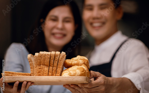 Happy Smiling Couple Presenting some Fresh Bread on Wooden Tray. Bake at Home. Closeup and Selective Focus