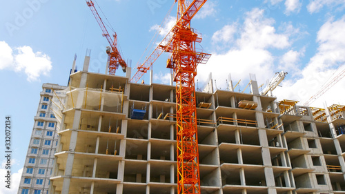 Two cranes near the building under construction on a background of a cloudy sky