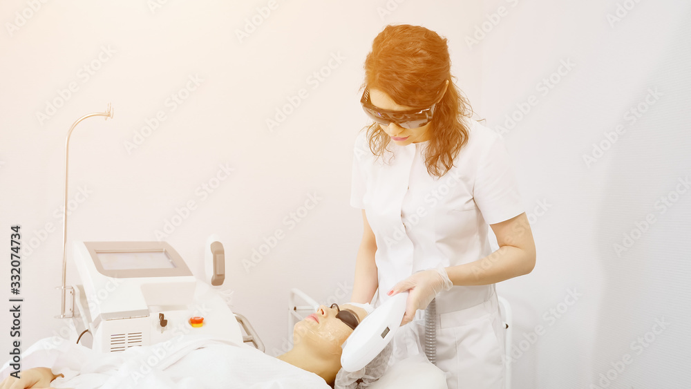 Obraz premium skilled therapist in white coat and black sunglasses makes laser hair removal on beauty salon patient face sunlight