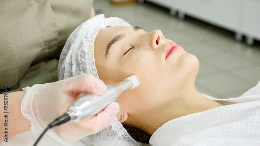 lady in green coat makes microdermabrasion procedure on face of beauty salon patient lying on white couch lady in green coat makes microdermabrasion procedure on face of beauty salon patient lying on white couch
