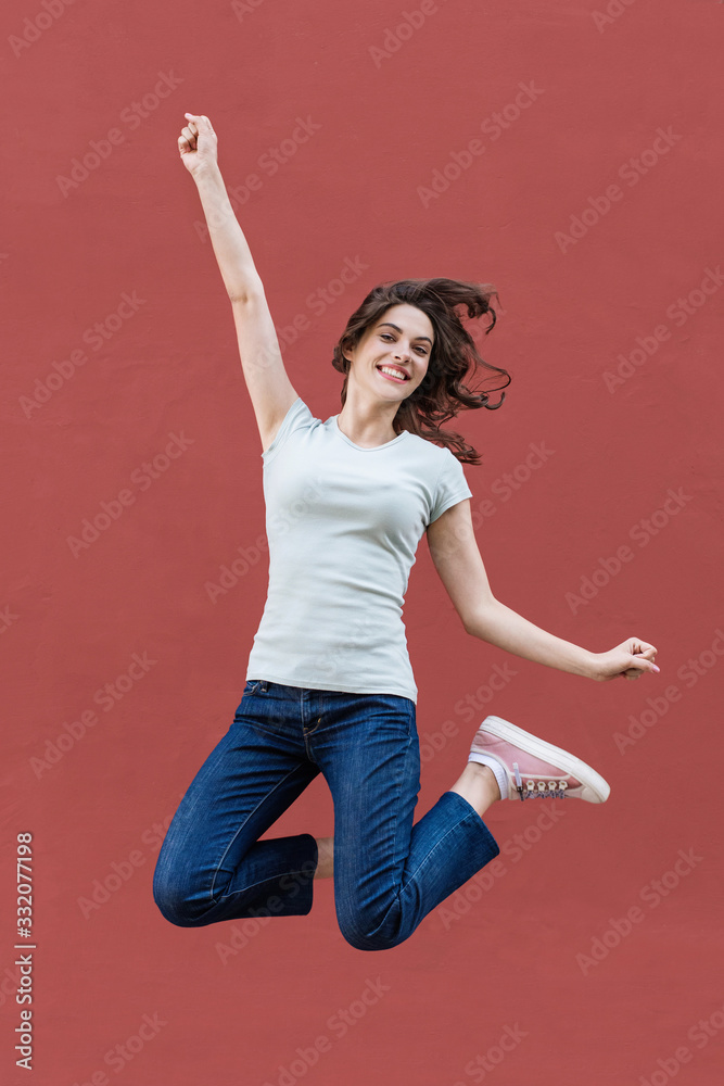 Joyful happy young woman jumping against red wall, beautiful girl enjoy life 