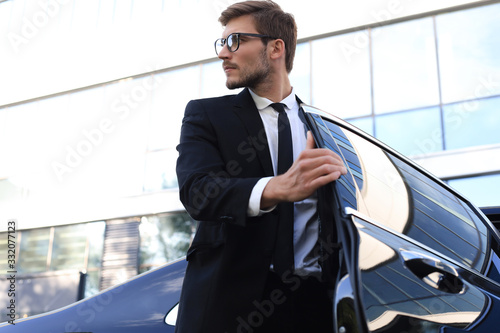 Handsome serious young businessman sitting into his comfortable new car and going to the office.