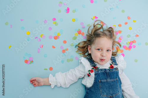 Funny little girl lies on a floor with a confetti pieces over her head