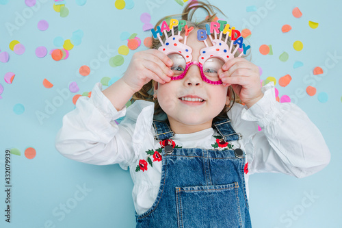 Happy little girl lies on a floor, holding onto her birthday glasses