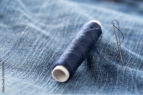 Blue yarn thread with needle on blue jeans denim close up - jeans fashion mending or repair concept