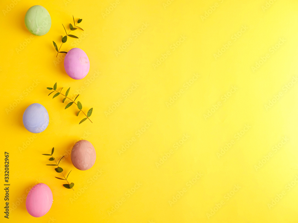 Flat lay composition of Happy Easter holiday concept. Colorful pastel egg with eucalyptus branch on yellow background. Copyspace, top view.