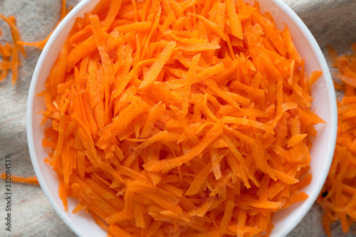Shredded carrots in a white bowl on cloth, view from above. Flat lay, top view, overhead. Close-up.