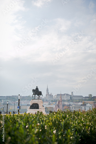 Monument to the horseman on the background of the panorama of Pest mountain and Fisherma's Bastion in Budapest with green leaves in the foreground near the Parliament photo