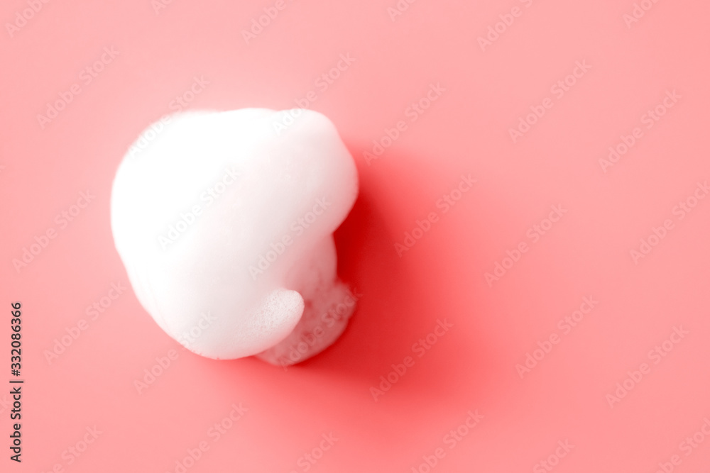 White foam smudge from soap, shampoo or cleanser on pink background with selective focus. Close-up, macro