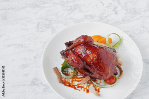  Baked quail in the oven with spices, herbs and fruits, served on a white plate with fruits and soy sauce.