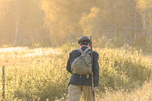 Fotografie A man with a backpack and a rifle on his shoulder is walking towards the forest