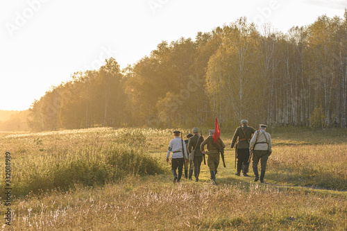 A group of red army soldiers with a red flag goes towards the forest. Historical reenactment © Vitalii