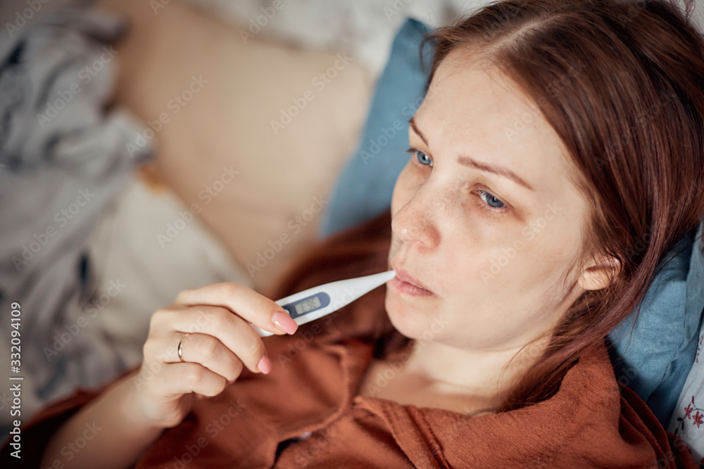 high temperature - the first sign of a viral disease, a woman measures the temperature with a thermometer high temperature - the first sign of a viral disease, a woman measures the temperature with a thermometer