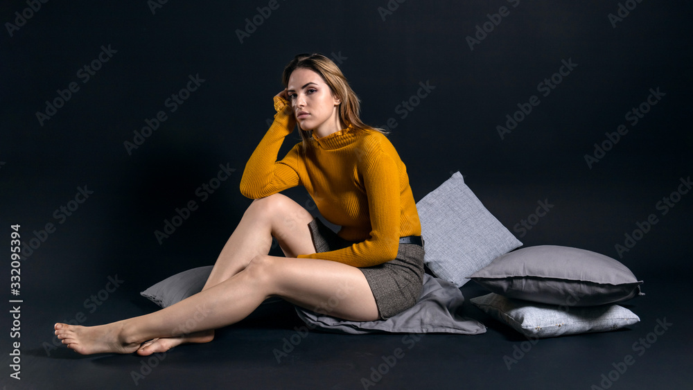 young pretty girl sitting on the floor among pillows on a dark background young pretty girl sitting on the floor among pillows on a dark background