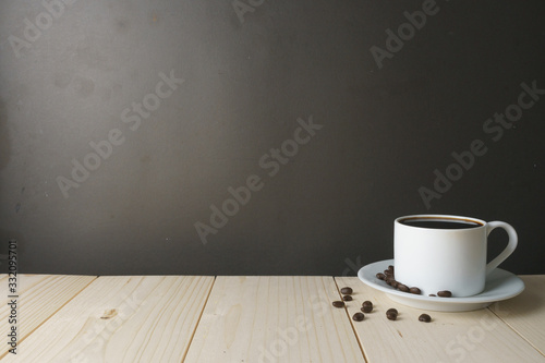coffee cup with beans on wooden desk against dark background. copy space for your text