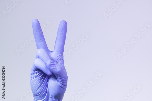 V sign is showed by right man hand in a purple medical glove on a white background. The symbol of Victory. Victory over a virus.