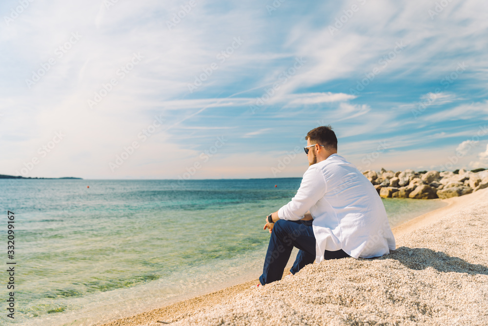 young stylish man sitting at sea beach enjoying the view