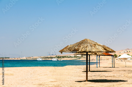 Sandy beach - Japanese Gardens in Jordan. A tropical beach with umbrellas made of dry palm leaves and views of the Red sea. © Mekhanik