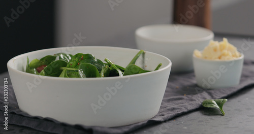 kumato tomatoes to fresh spinach leaves into white bowl to make a salad