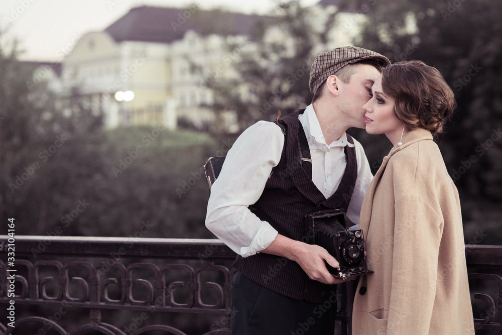 A young man and woman stand in a Park near a metal fence and hug, a man holding a retro camera in his hands.historical reconstruction