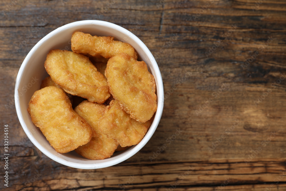 Bucket with tasty chicken nuggets on wooden table, top view. Space for text Bucket with tasty chicken nuggets on wooden table, top view. Space for text