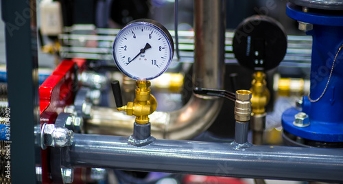 pressure gauge psi meter in pipe and valves of water system industrial focus left closeup white light defocus blur background