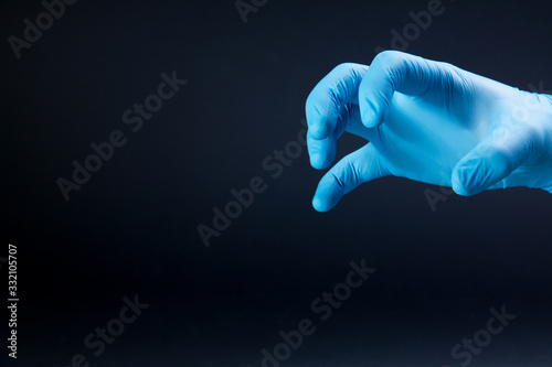 A man hand in a blue medical glove as a claw scares virus on a black background