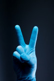 V sign is showed by right man hand in a blue medical glove on a black background. The symbol of Victory. Victory over a virus.