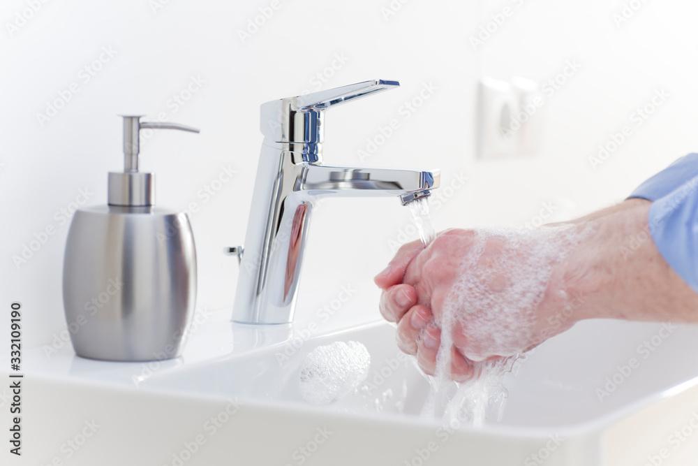 Man washing his hands with liquid soap in a white bathroom to protect himself against infection Man washing his hands with liquid soap in a white bathroom to protect himself against infection