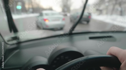 Close up of driver's hands on steering wheel. Driver turns left on crossroad. Blurred view of car in front. View through windscreen.