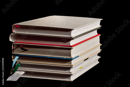 Many hardcover books on black background. Stack of books with white and yellow pages.