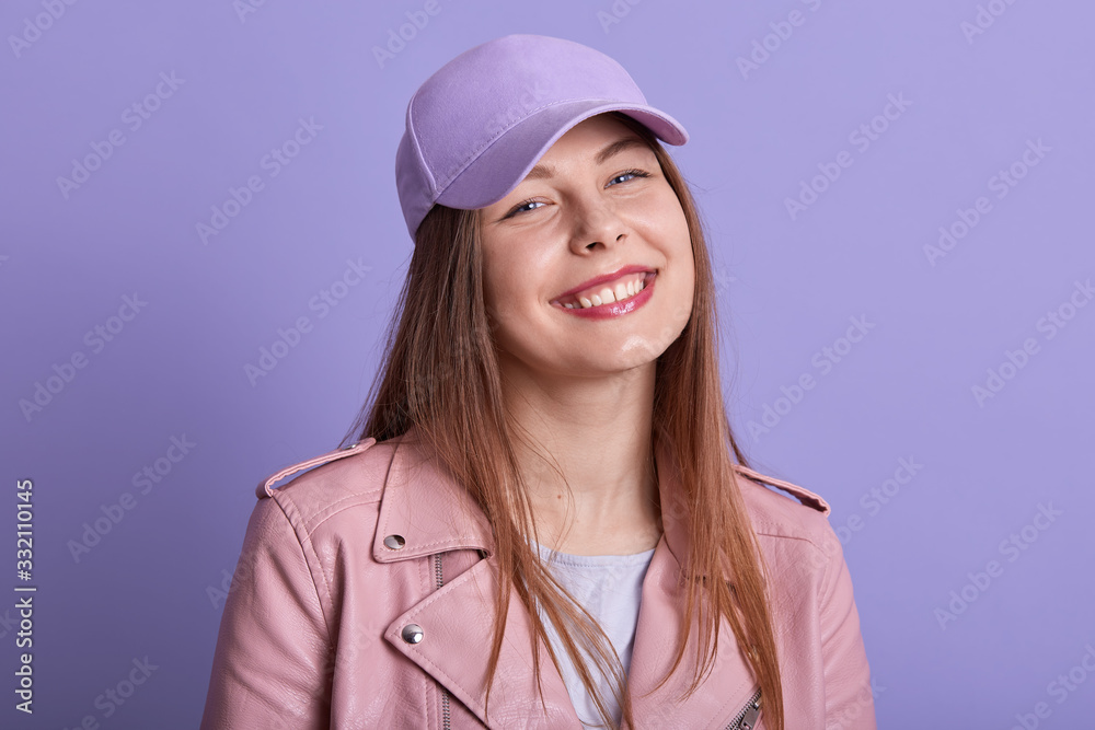 Close up portrait of charming beautiful young female smiling sincerely, being in good mood, standing isolated over lilac background in studio, feeling well, having satisfied facial expression. Close up portrait of charming beautiful young female smiling sincerely, being in good mood, standing isolated over lilac background in studio, feeling well, having satisfied facial expression.