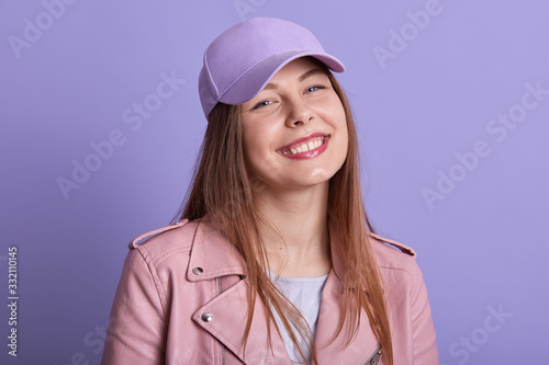 Close up portrait of charming beautiful young female smiling sincerely, being in good mood, standing isolated over lilac background in studio, feeling well, having satisfied facial expression.