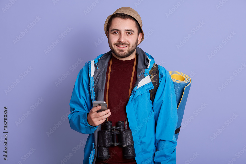 Close up portrait of young handsome men with backpack holding smart phone. Smiling student traveler portrait. Cheerful man posing isolated over lilac background. Lifestyle and people concept. Close up portrait of young handsome men with backpack holding smart phone. Smiling student traveler portrait. Cheerful man posing isolated over lilac background. Lifestyle and people concept.