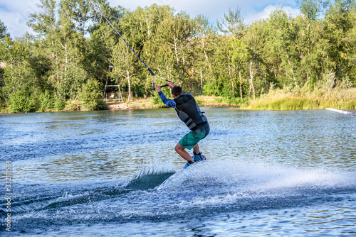 Man wakeboarding on river lake sea on summer spring day in jacket. Soft focus. Action blur.